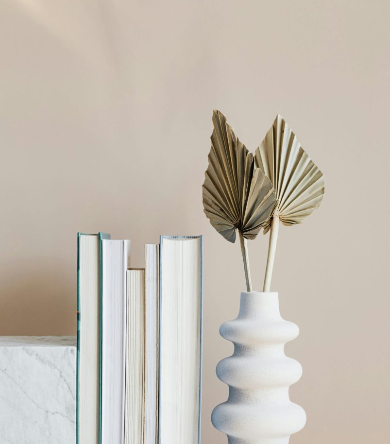Elegant minimalist bookshelf decor featuring a stylish vase with dried leaves and neatly arranged books.